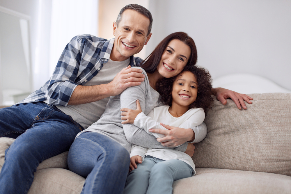 curly-haired girl smiling and sitting on the couch with her parents