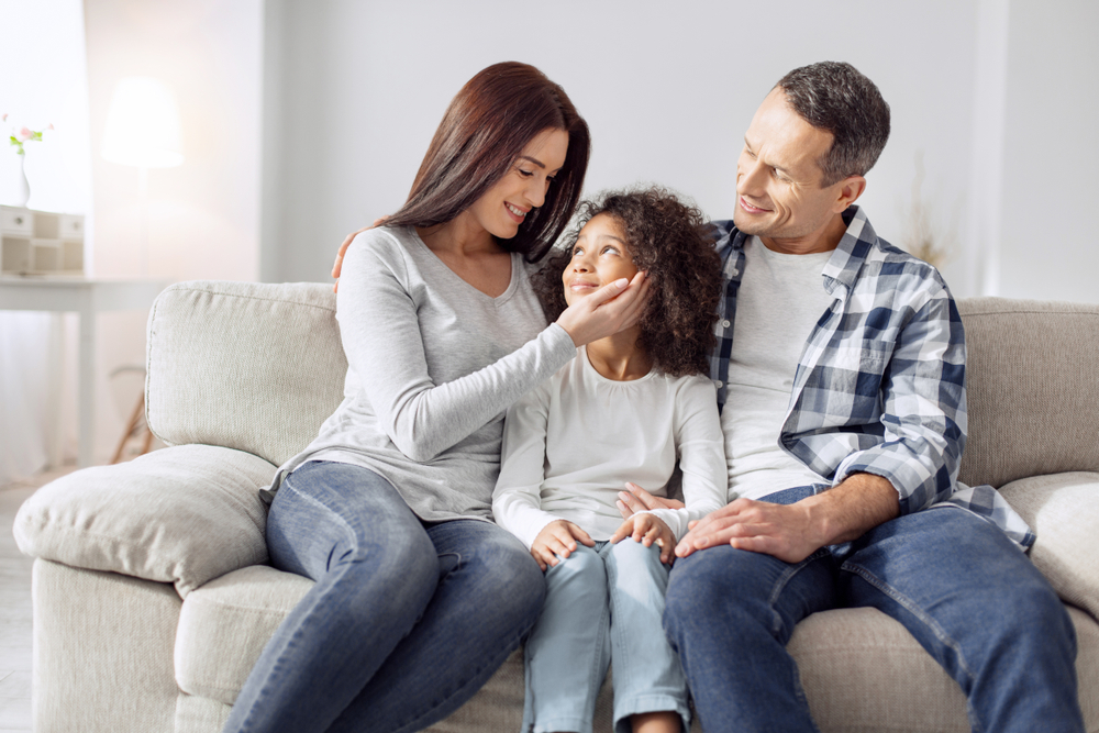attractive alert curly-haired girl smiling and sitting on the couch with her pa