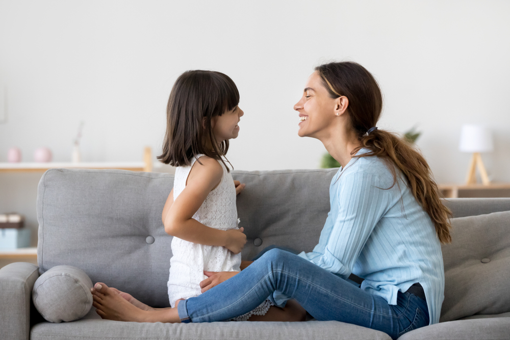attractive woman and little girl sitting on comfortable couch at hom