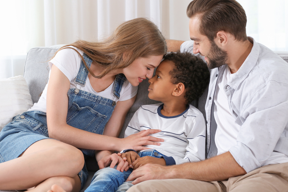happy couple with adopted African-american boy sitting on couch at home