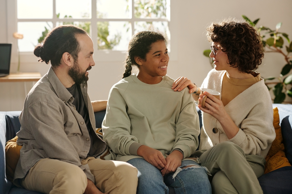 Happy parents talking to their adopted daughter while sitting on sofa in the living room