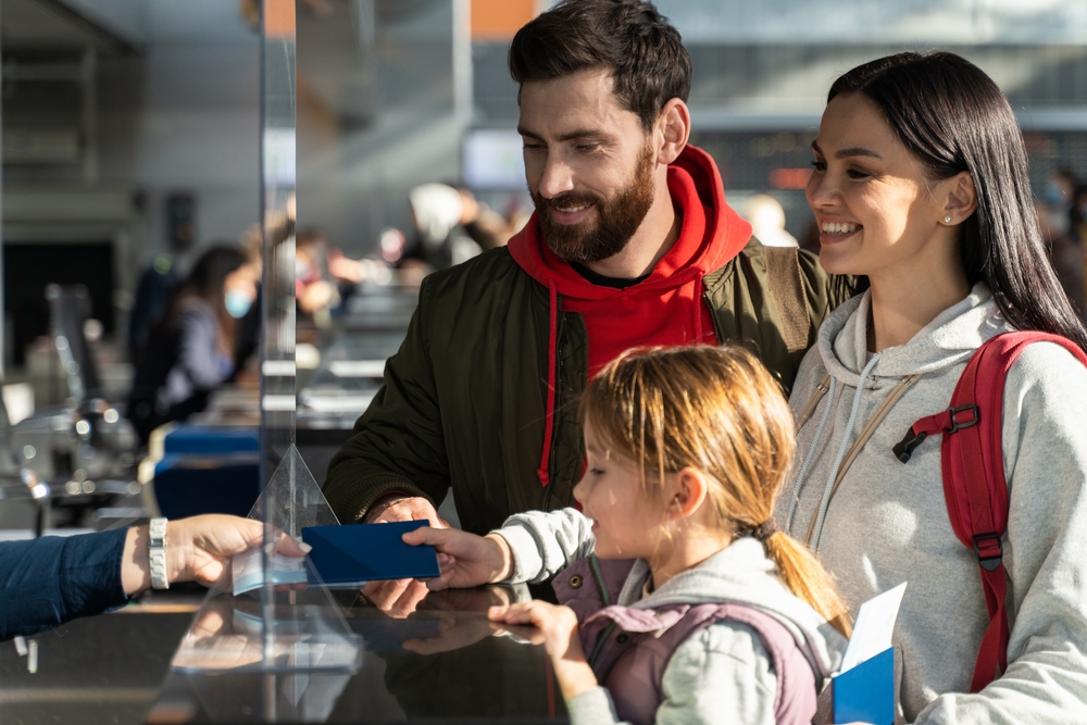Unrecognizable employee of airport checking passports and biometric data while working with family of passengers