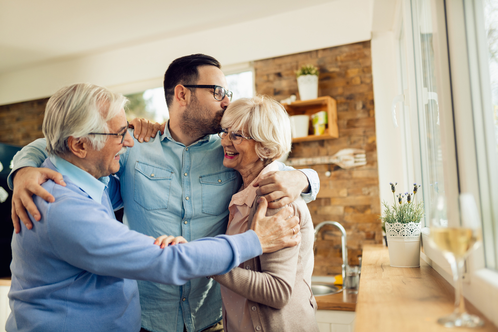 Happy mature couple embracing their adult son while greeting with him in the kitchen