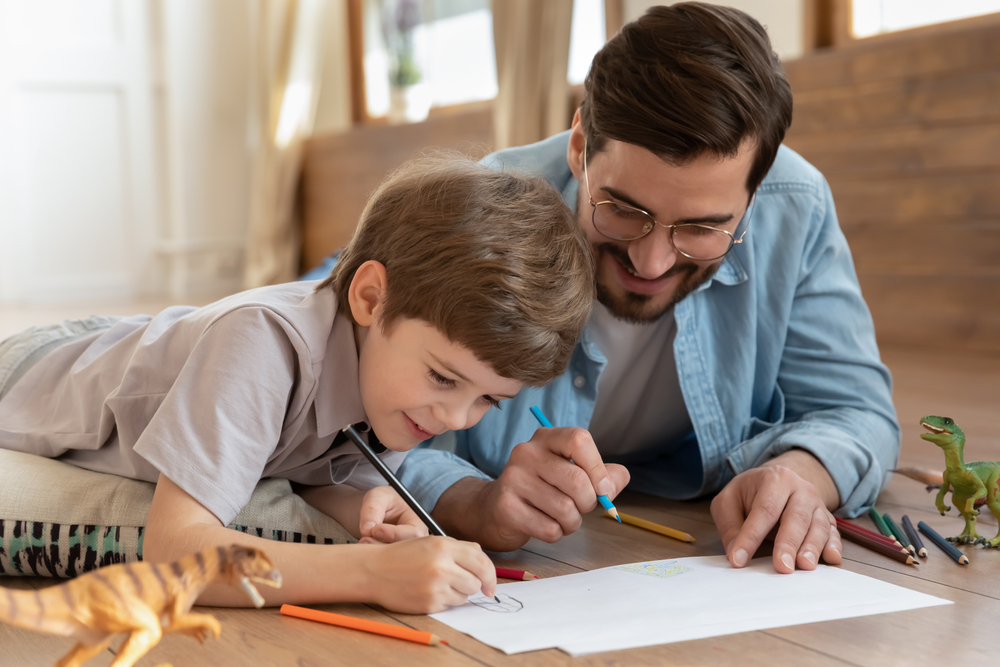 Happy playful dad drawing in album with excited small boy child on weekend at home
