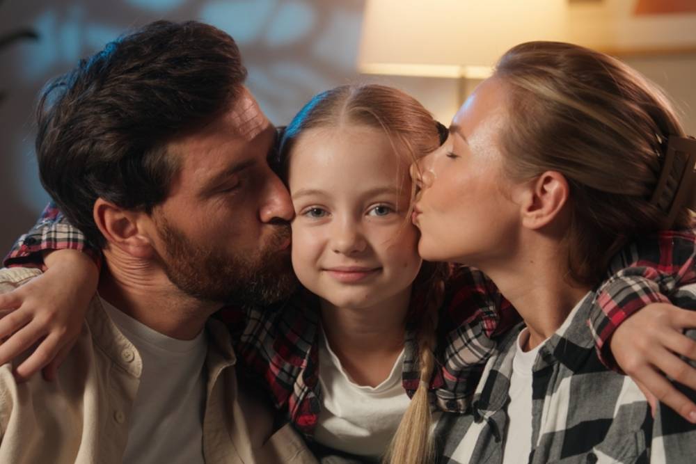 parents kissing daughter in cheeks love kiss parenting concept love bonding affectionate smiling looking at camera satisfied parents with child girl kid adopt custody