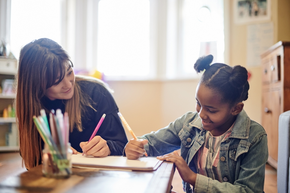 Learning, adoption and mother with black girl writing in home for homework, drawing and homeschool