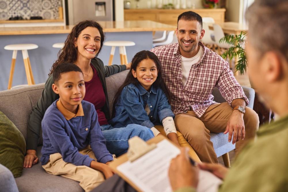 Smiling parents with adopted children discussing with social worker at home while looking at him.